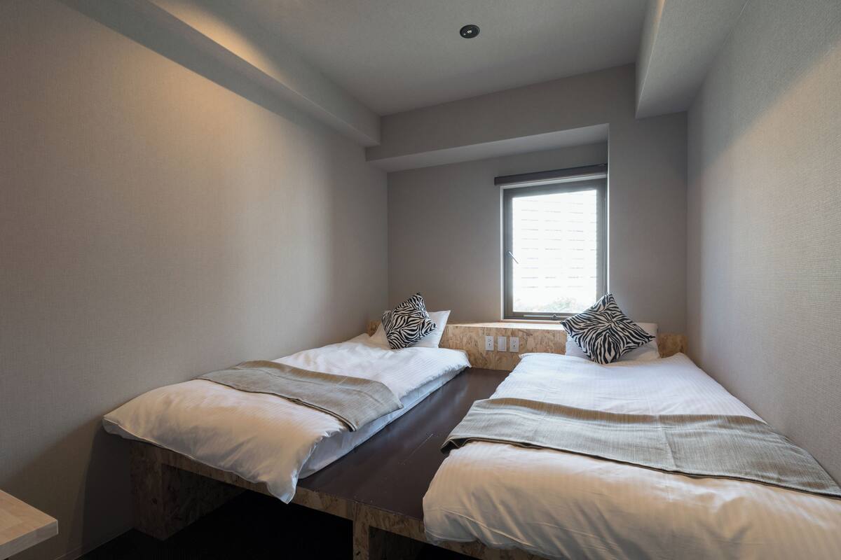 A bedroom with two beds, a window, and a wooden bench.