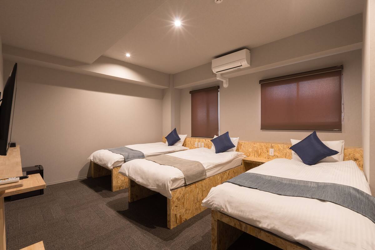 A hotel room with three wooden beds, a flat-screen TV, and an air conditioning unit.