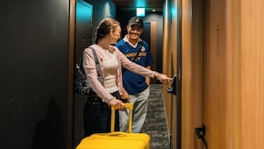 A hallway with wooden doors, a yellow suitcase, and a person in a blue shirt. - 3U NAMBA MINAMI - DOYANEN HOTELS (Osaka)