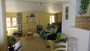 Una sala de estar acogedora con un sofá, una mesita, una silla y un ventanal con cortinas.
