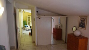 Un pasillo estrecho con un aparador de madera y un espejo a la derecha, que da a una habitación con cama y sillón.