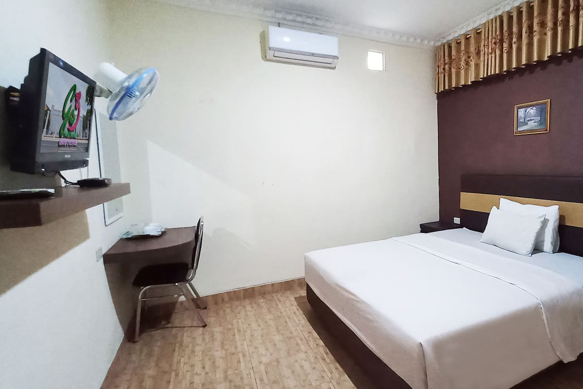 Ein Hotelzimmer mit einem Bett, einem Schreibtisch mit Stuhl, einem Fernseher und einer Wandklimaanlage.