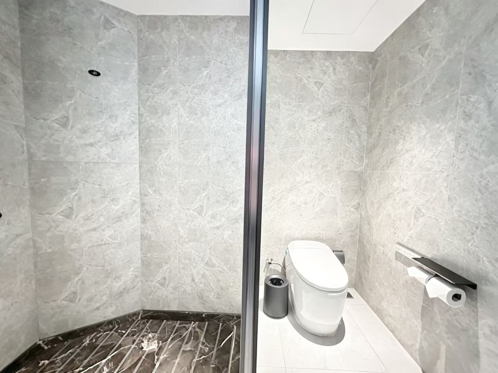 A bathroom with a toilet, a trash bin, and a shower area.