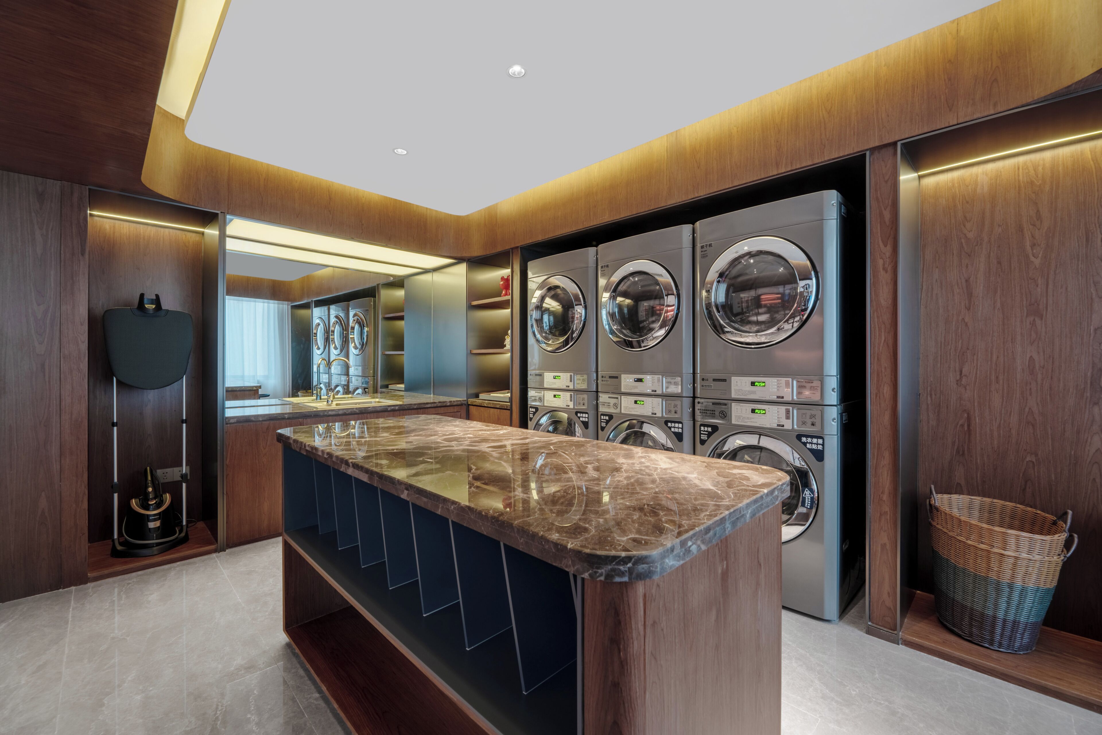 A modern bathroom with a marble countertop, multiple washing machines, and a large mirror.