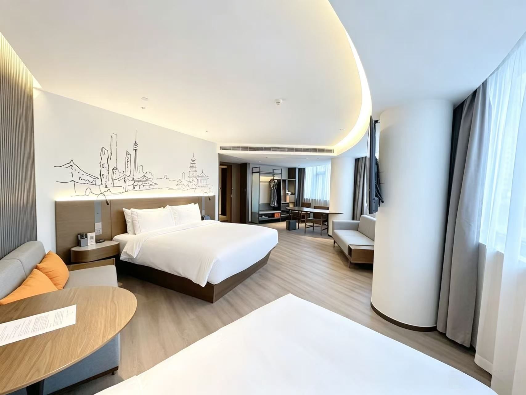 A modern hotel room with a large bed, a seating area with a table, and a cityscape mural on the wall.