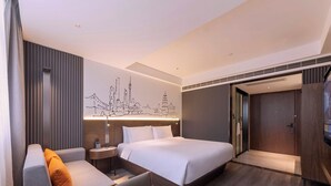 Ein modernes Hotelzimmer mit Bett, einer Couch, einem kleinen Tisch und einem an der Wand hängenden Kunstwerk, das eine Stadtansicht zeigt.
