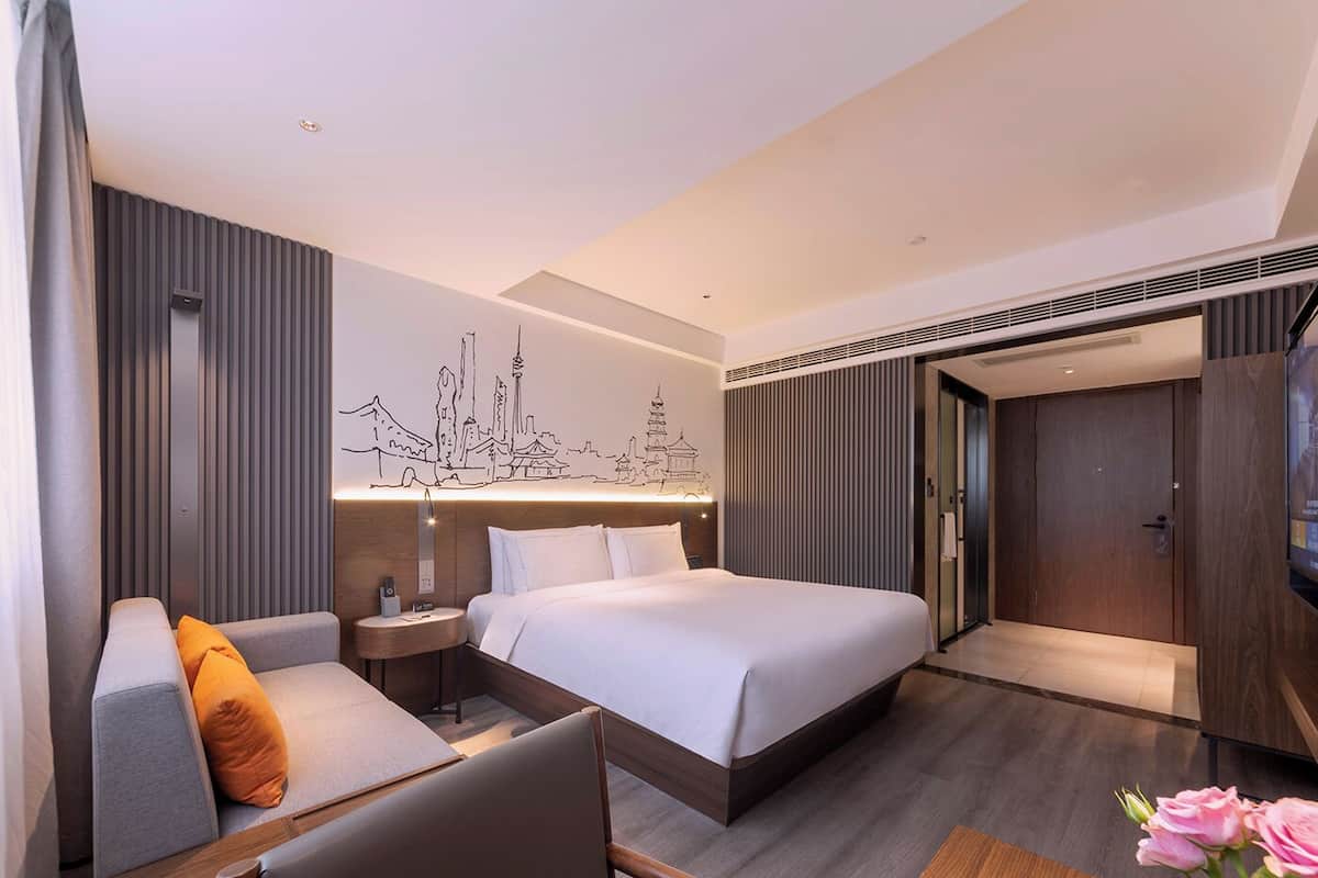 Una habitación de hotel moderna con una cama, un sofá, una mesita y una obra de arte en la pared que representa un paisaje urbano.