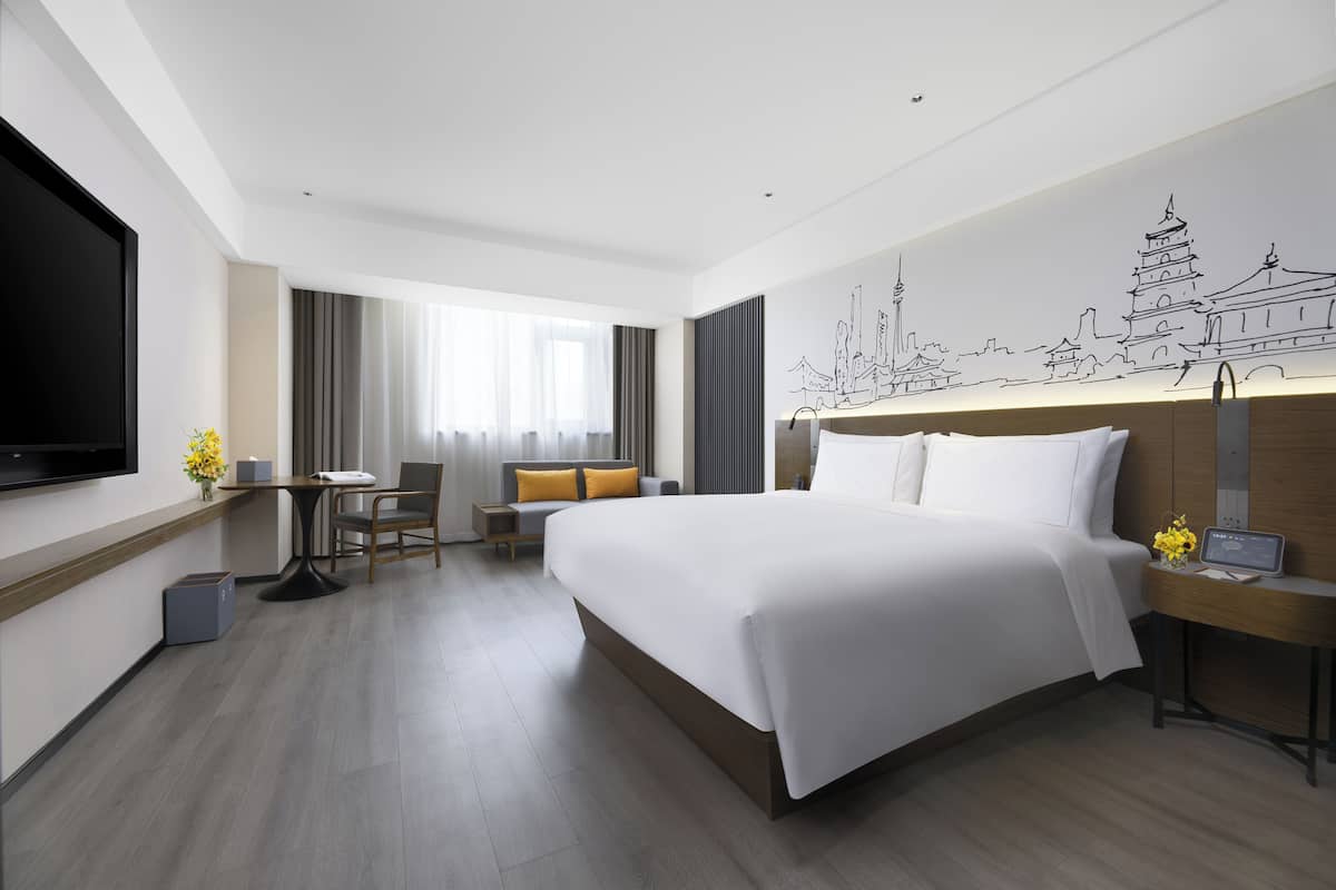 Una habitación de hotel moderna con una cama grande, un escritorio, una silla, un televisor y un mural en la pared.