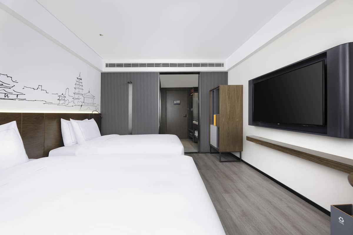 Una habitación de hotel moderna con una cama grande, un televisor de pantalla plana, un aparador de madera y un televisor montado en la pared.