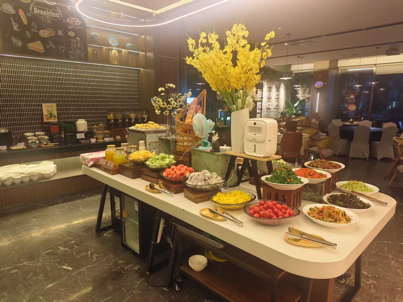 A buffet setup with various food items and a decorative vase of yellow flowers.