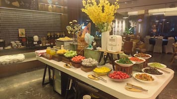 A buffet setup with various food items and a decorative vase of yellow flowers.