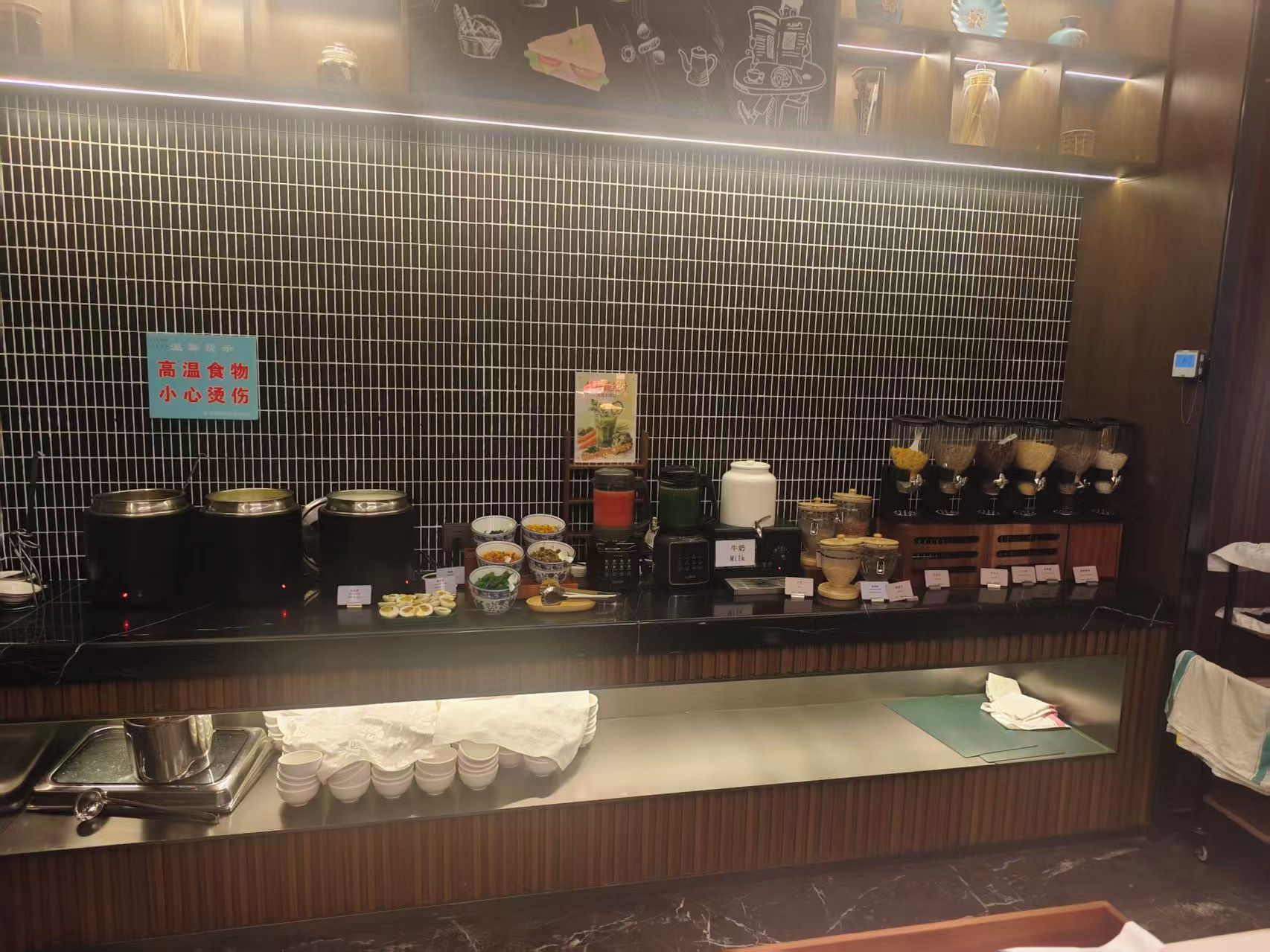 Zona de bufé con varios recipientes de comida y un cartel que indica alimentos de alta temperatura.