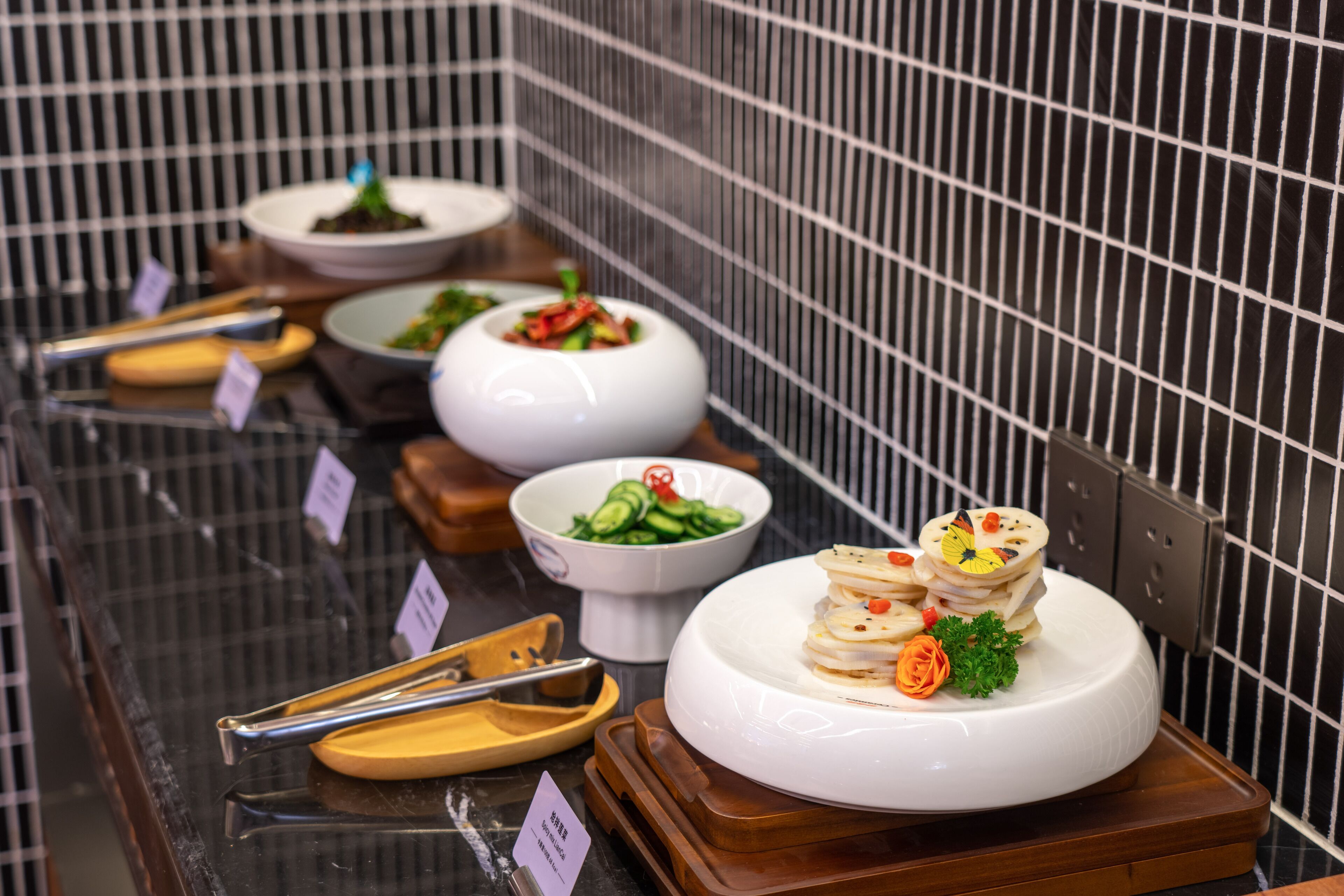 A buffet with various dishes, including a central white bowl with a stack of pancakes, surrounded by smaller bowls of different foods.