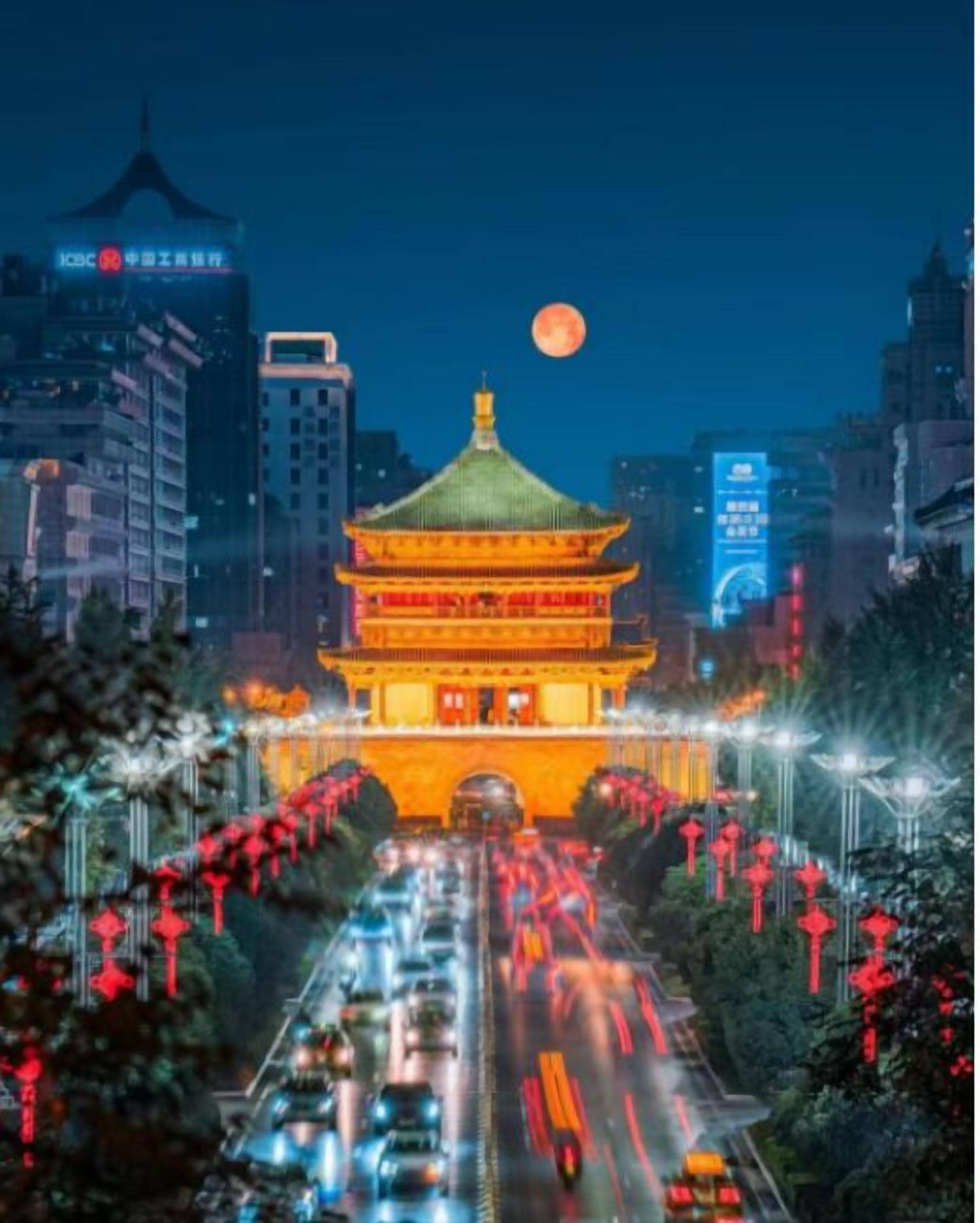 A traditional Chinese building with a green roof and red lanterns, surrounded by modern buildings and a busy road.