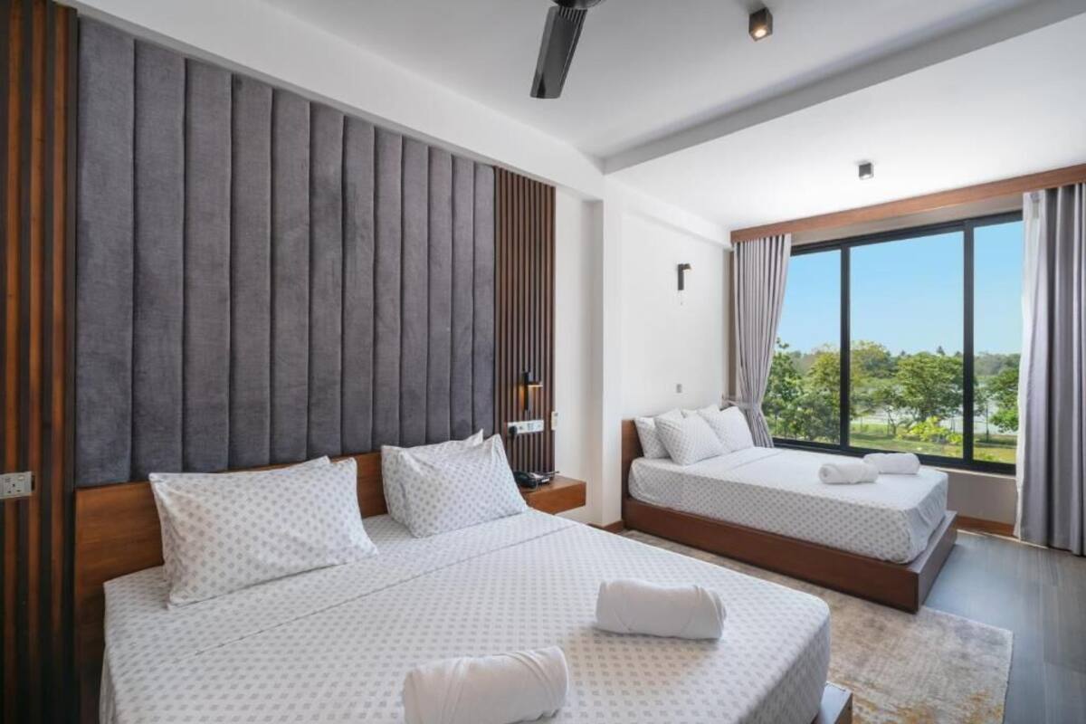 A modern hotel room with two beds, a large window with a view, and a wooden accent wall.