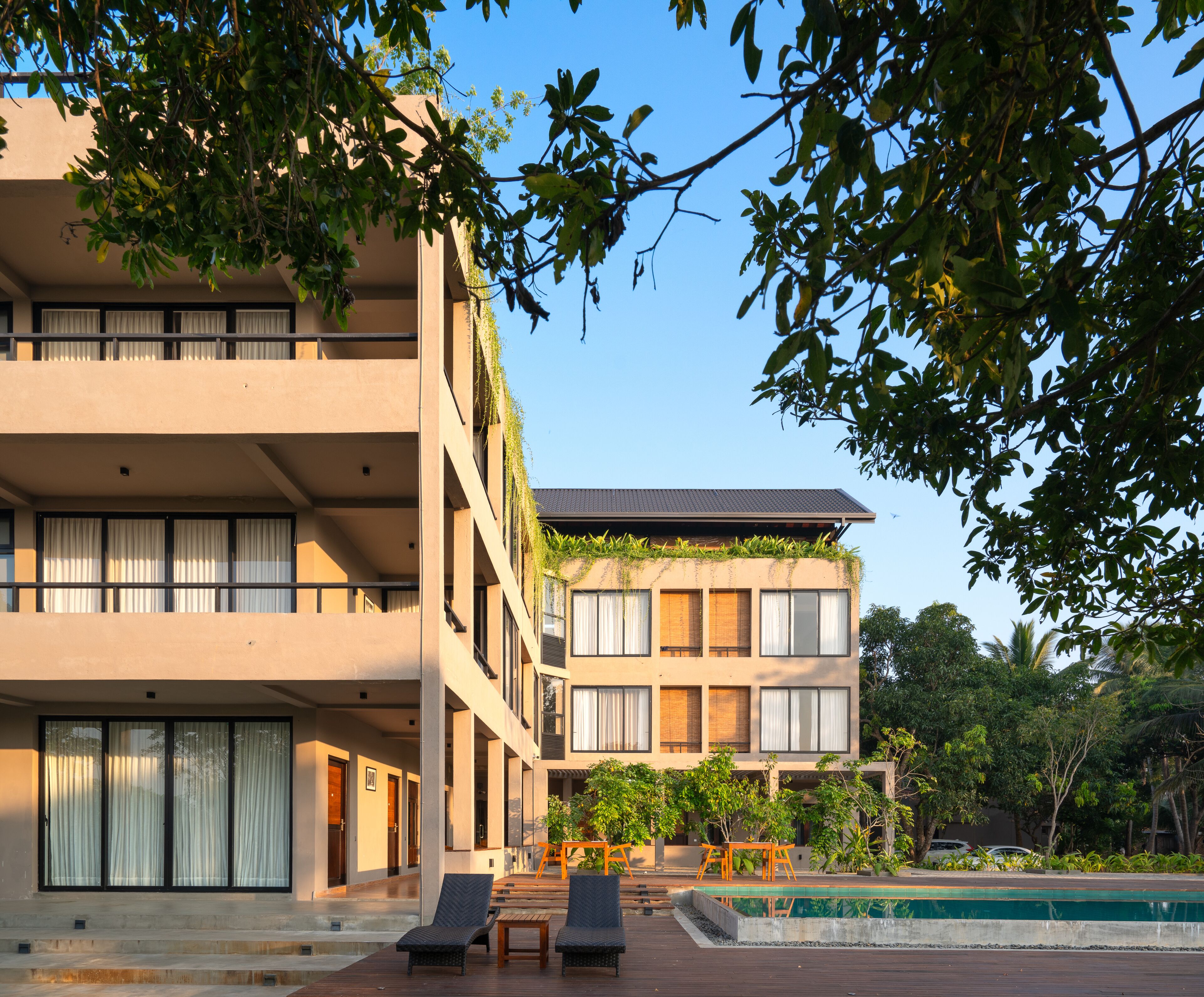 A modern hotel with a pool area, outdoor seating, and lush greenery.