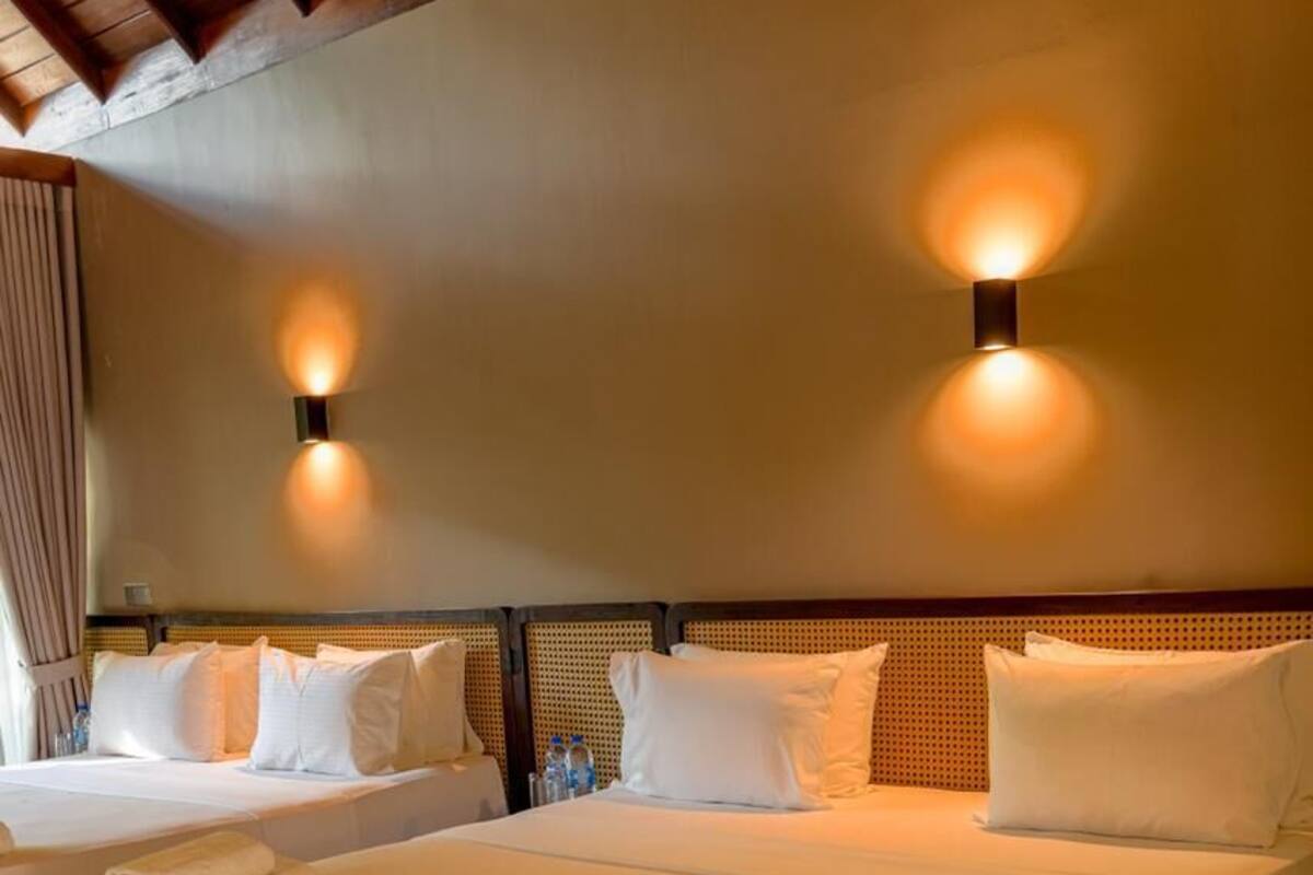 A hotel room with two beds, a wooden ceiling, and wall-mounted lighting.