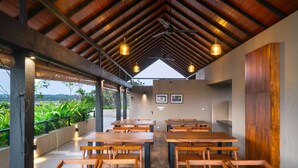 Un restaurante con mesas y sillas de madera, un techo alto con vigas a la vista, iluminación colgante y cuadros en la pared.