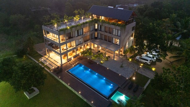 Un edificio moderno de varios pisos con jardín en la azotea, una piscina y un área exterior bien iluminada.