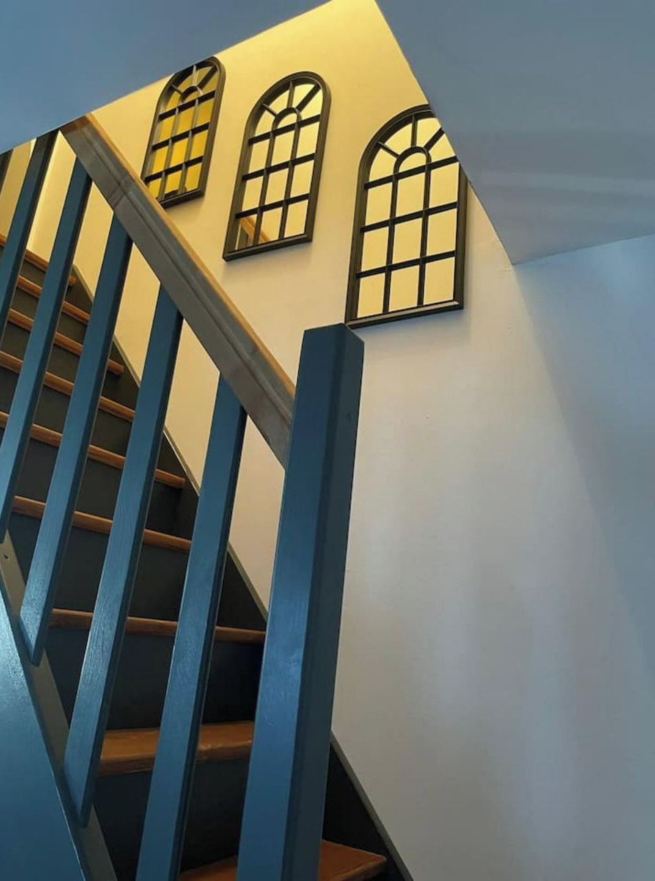 Een trap met blauwe leuningen en drie boogvensters in de muur.