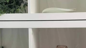 A white shelf unit with a green plant, a white plate, and a red vase.