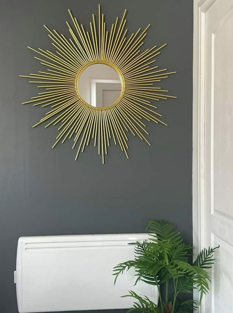 Ein Sonnenstrahl-Spiegel mit goldener Rahmung an einer dunklen Wand.