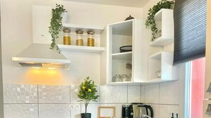 Una cocina moderna con armarios blancos, horno empotrado, lavavajillas, lavadora y una ventana con persianas.