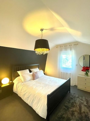 A bedroom with a bed, bedside lamp, and a hanging light fixture. - Liva-blom (Guesnain)