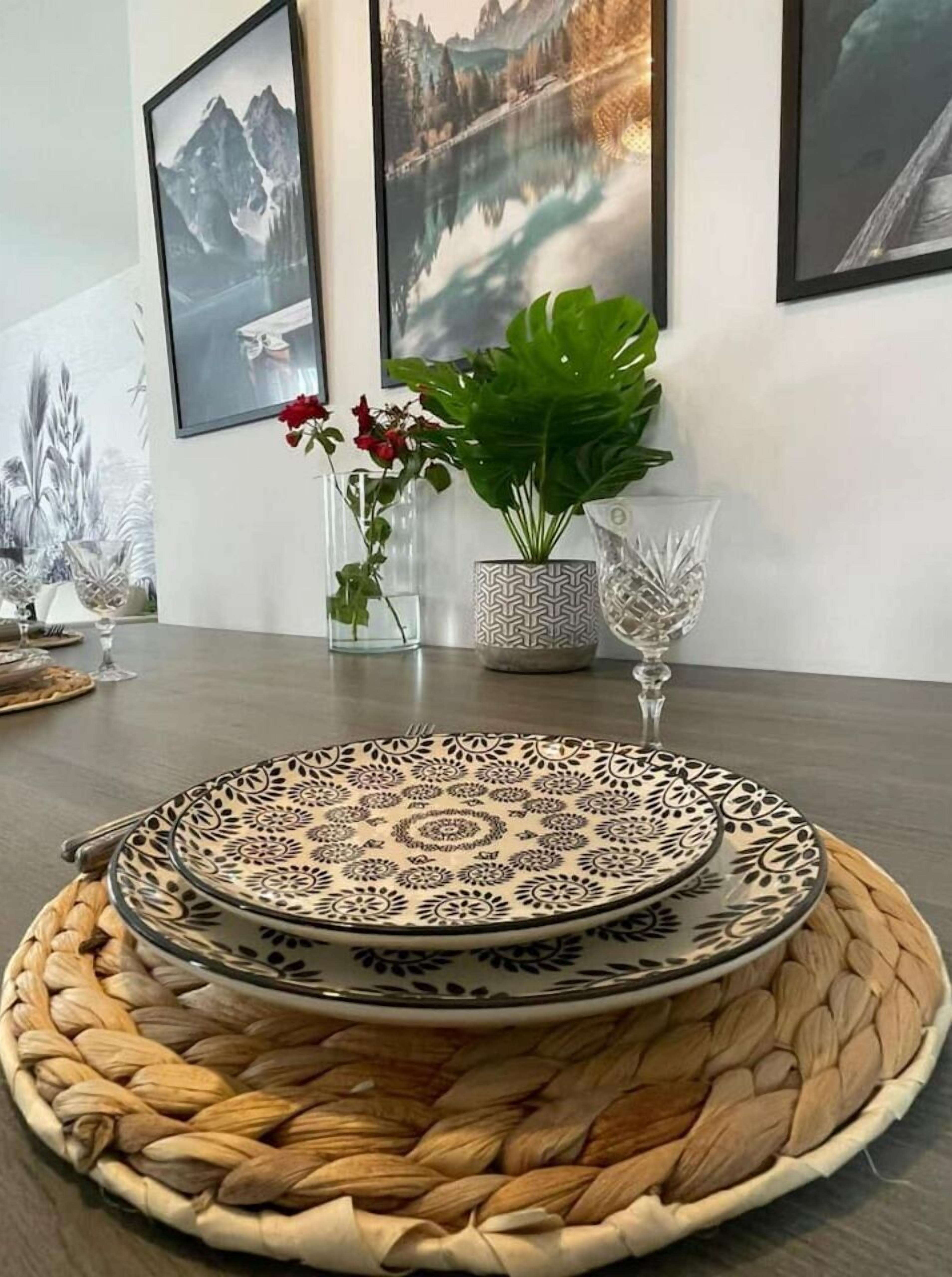 A dining table with a woven placemat, a decorative plate, and a vase with red flowers.