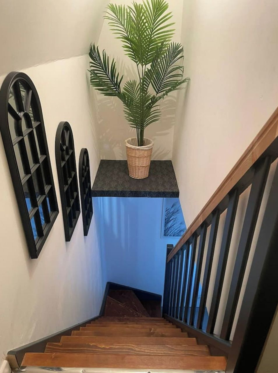 A staircase with wooden steps and a black railing, leading to a landing with a potted plant and decorative wall sconces.