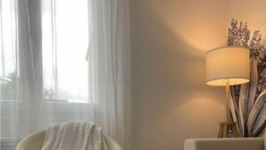 Un salón acogedor con una butaca moderna, una mesa con una bandeja que sostiene una tetera y un libro, y una lámpara sobre una mesita auxiliar.