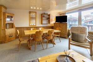 A wooden dining area with a table and chairs, a television, and a large window with a view of buildings.