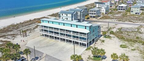 A beachfront hotel with a large building, a parking area, and a sandy beach.