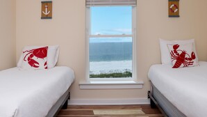 Ein Schlafzimmer mit zwei Betten, einem Fenster mit Meerblick und zwei Wanddekorationen.