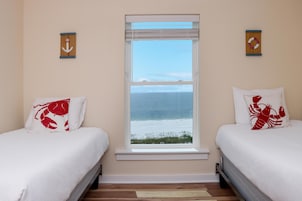 A bedroom with two beds, a window with a view of the sea, and two wall-mounted decorative items.