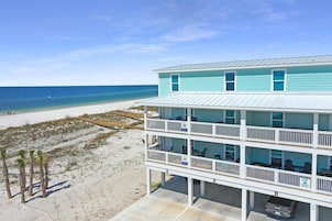 Edificio frente a la playa con varios pisos y balcones, un Jeep estacionado en la entrada, y una playa de arena al fondo.