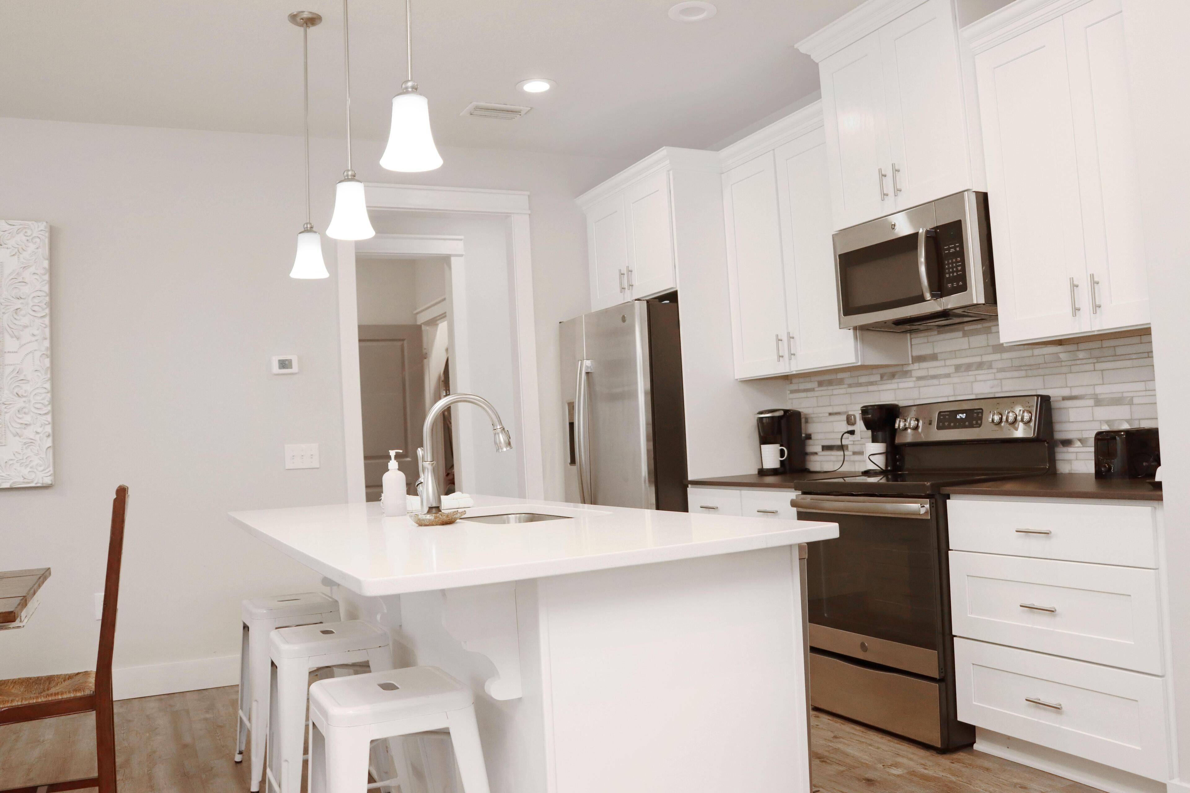 Una cocina moderna con armarios blancos, electrodomésticos de acero inoxidable e iluminación colgante.