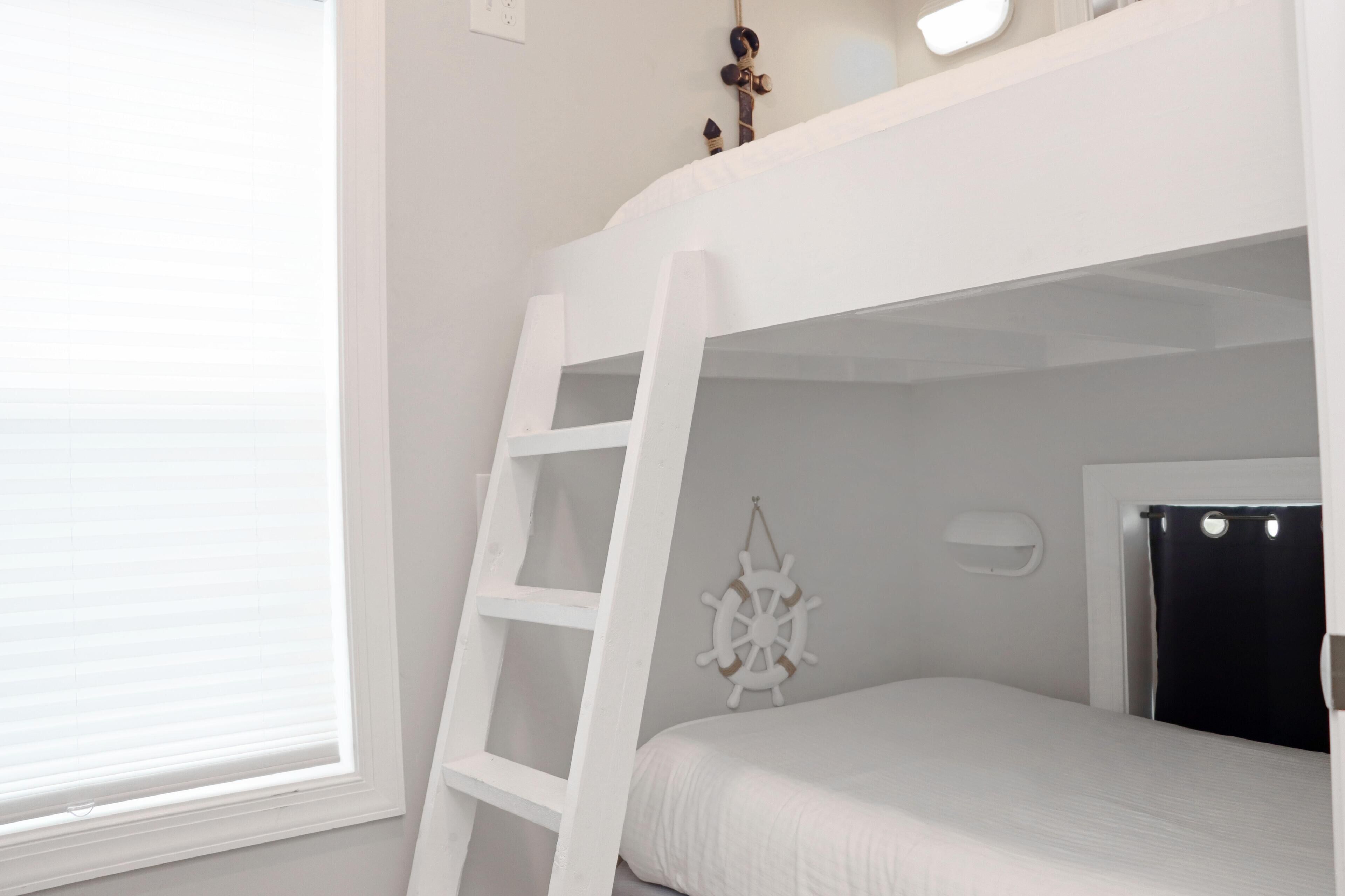 A bunk bed with a ladder, a ship's wheel decoration, and a black curtain.