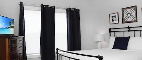 A bedroom with a bed, a dresser, a television, and a window with curtains.