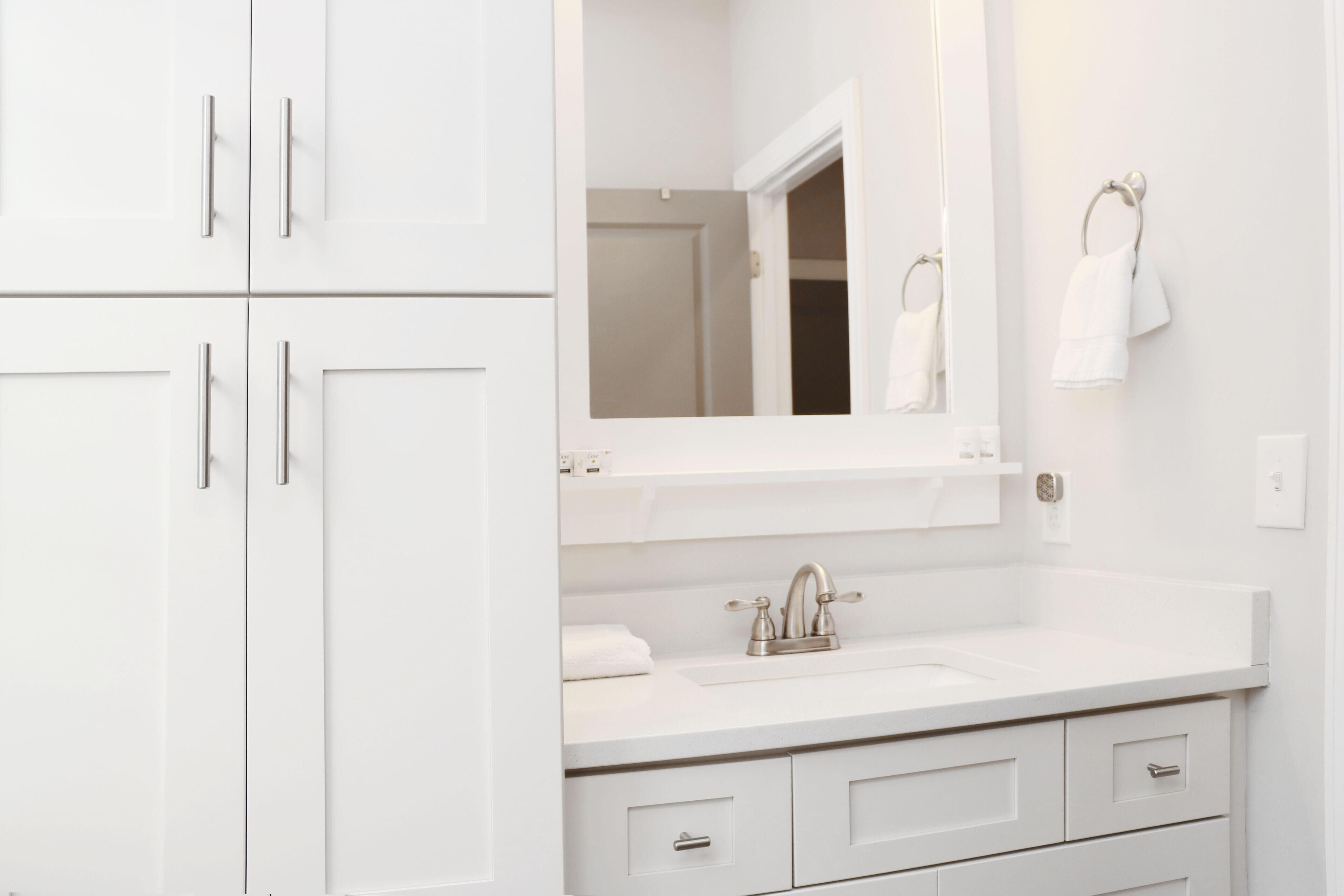 A modern bathroom with white cabinetry, a sink with a mirror above it, and a towel rack on the wall.