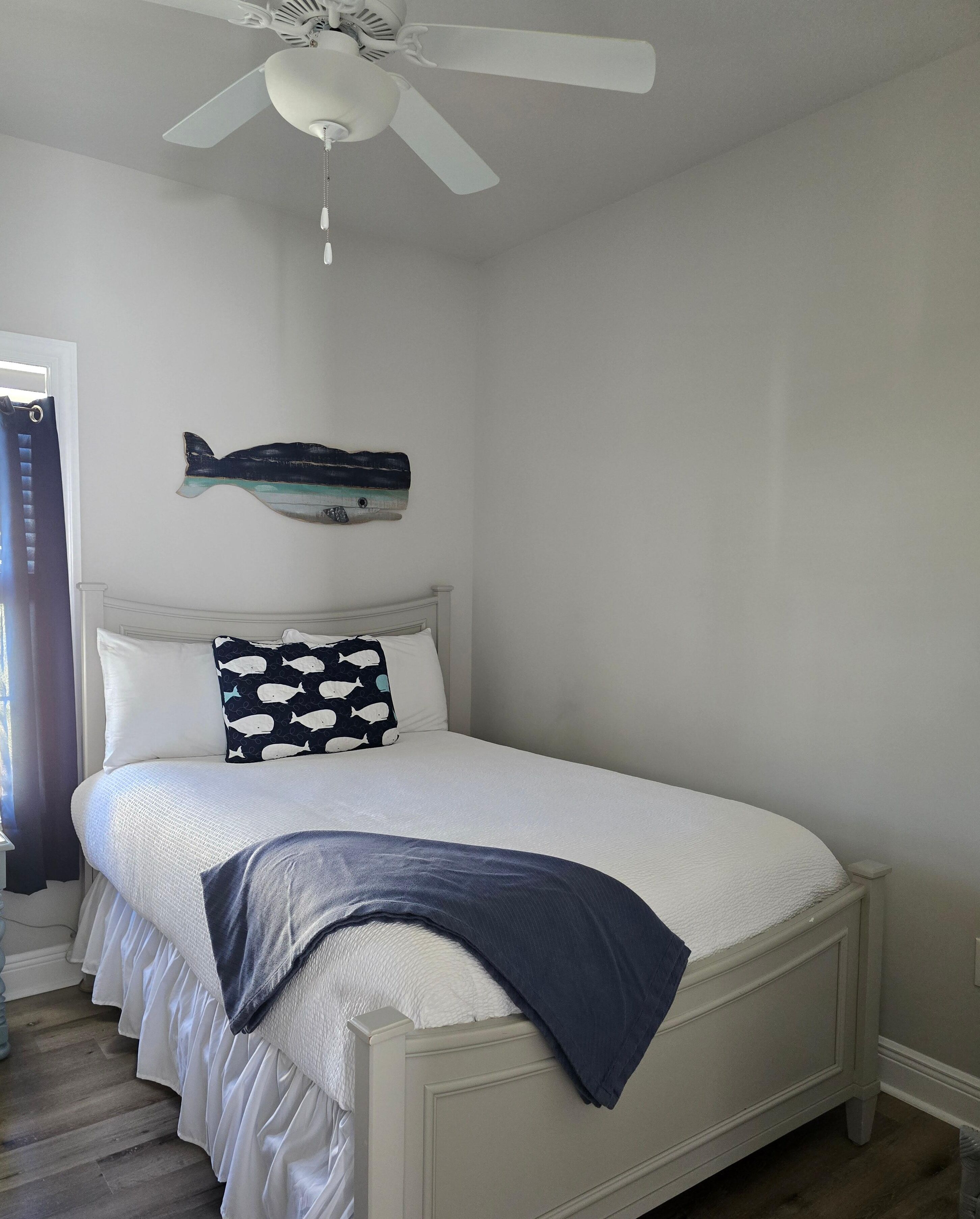 Une chambre à coucher avec un lit, un ventilateur de plafond et un décor mural représentant des poissons.