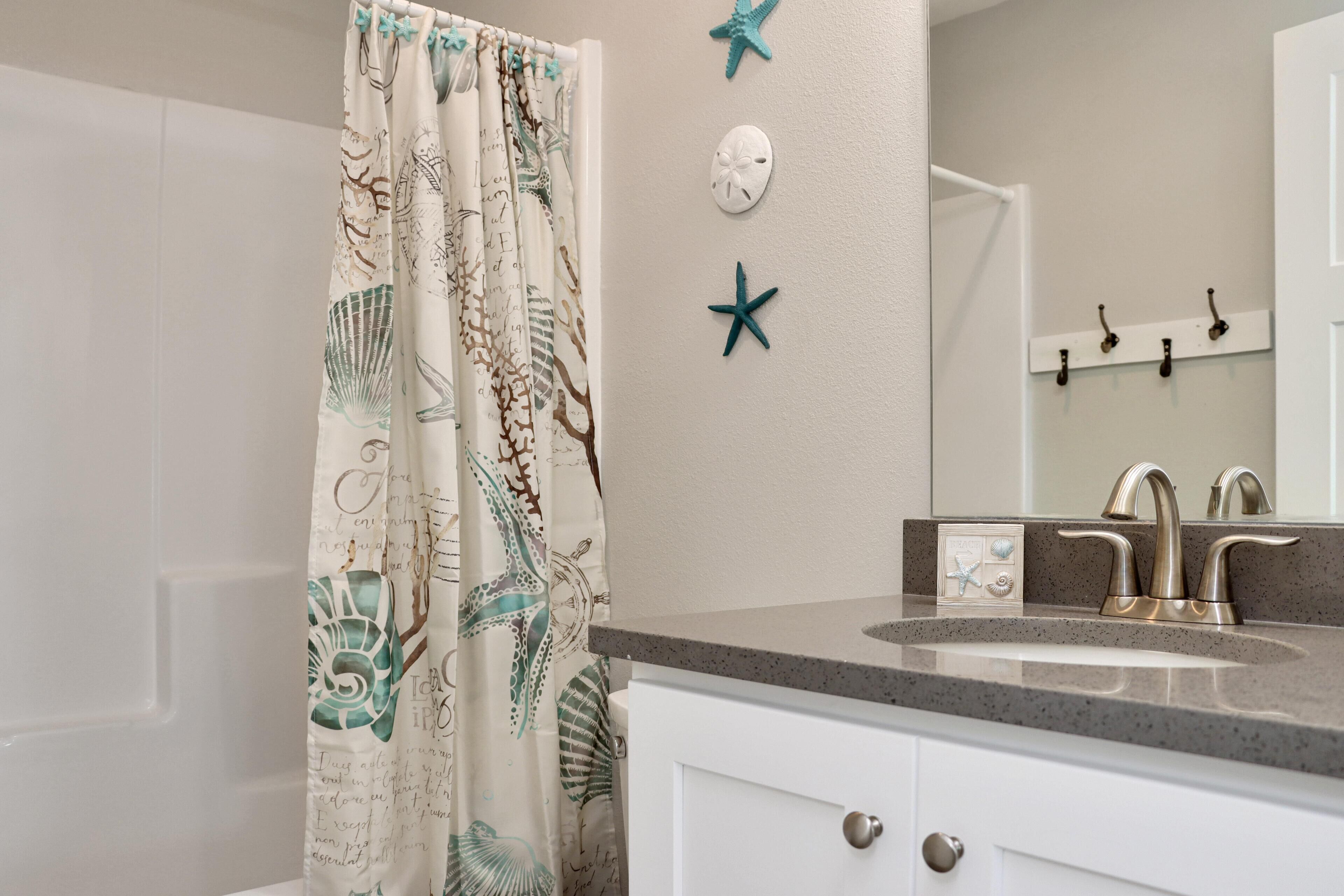 Une salle de bain avec un rideau de douche orné de motifs d’animaux marins, un lavabo doté d’un robinet moderne et un miroir fixé au mur.