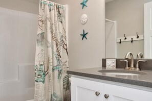 A bathroom with a shower curtain featuring sea creature designs, a sink with a modern faucet, and a wall-mounted mirror. - Pelican Roost A (Port St. Joe)