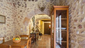 A stone-walled dining area with a wooden table, chairs, a basket of fruit, and a glass cabinet. - Holiday Home 'Siglo 16 Denia' with Private Terrace, Wi-Fi and Air Conditioning (Denia)