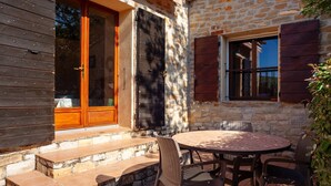A stone building with a wooden door and window shutters, a round table with chairs, and a small outdoor seating area. - Holiday Apartment "Les Cigales" with Mountain View, Private Garden & Wi-Fi (Ceyreste)