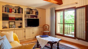 A cozy living room with a bookshelf, a television, a sofa, and a table with a tablecloth. - Holiday Apartment "Les Cigales" with Mountain View, Private Garden & Wi-Fi (Ceyreste)