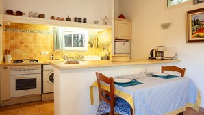 A kitchen with a dining table, a washing machine, a stove, and a window. - Holiday Apartment "Les Cigales" with Mountain View, Private Garden & Wi-Fi (Ceyreste)