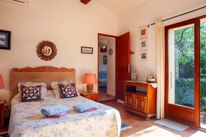 Quarto com cama, abajures, cômoda de madeira, espelho e porta que dá para uma varanda.
