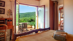 Ein Schlafzimmer mit Bett, Schreibtisch, Stuhl und Blick auf einen Balkon mit Tisch und Stühlen.