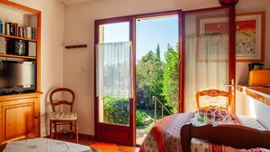 Ein Zimmer mit einer Schiebetür zu einem Garten, einem Bücherregal aus Holz, einem Sessel, einem Tisch mit Tischdecke und einem Bett.